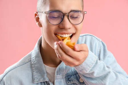 Young man eating French fries on pink background, closeupの写真素材