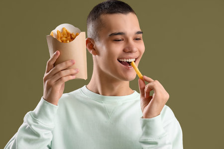 Young man eating French fries on color background, closeupの写真素材