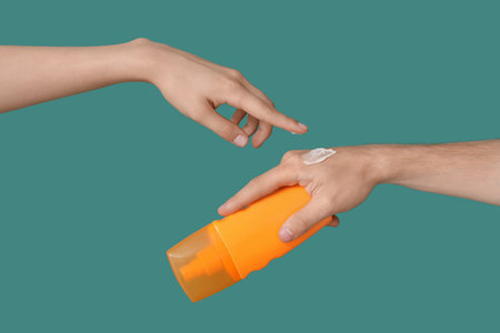 Woman applying sunscreen cream on hand against green backgroundの写真素材