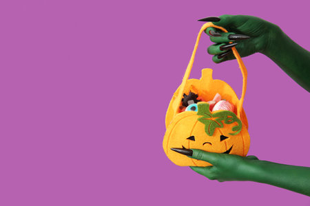 Green hands of witch with bag and candies on purple background. Halloween celebrationの写真素材