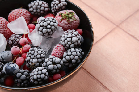 Bowl of frozen berries with ice on color tile background, closeupの写真素材
