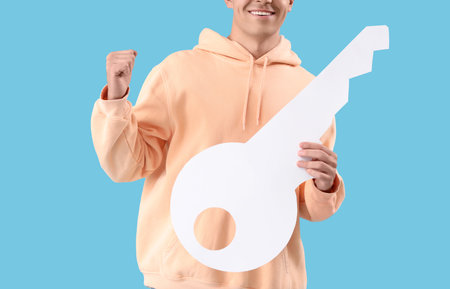 Happy young man with paper key on blue background, closeupの写真素材