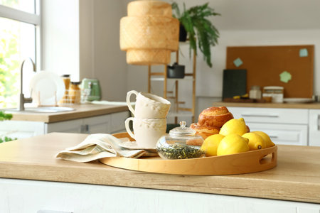 Tray with cinnamon rolls, cups, lemons and tea leaves on wooden countertop in modern kitchenの写真素材