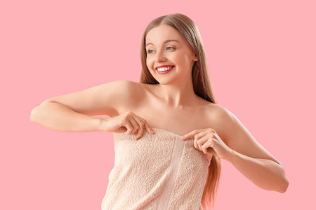 Pretty young woman wrapped in towel on pink backgroundの写真素材