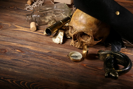 Human skull with pirate hat, golden nuggets, compass and sword on brown wooden backgroundの写真素材