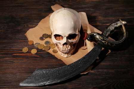 Human skull with sword, scroll and coins on brown wooden backgroundの写真素材