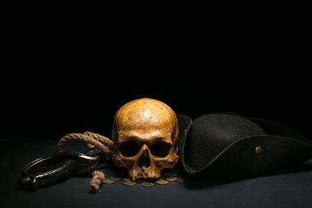 Human skull with sword, toy model of cannon, pirate hat and coins on black backgroundの写真素材