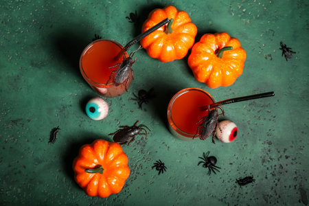 Composition with glasses of delicious bloody Mary cocktail, insects, pumpkins and tasty candies for Halloween on green backgroundの写真素材