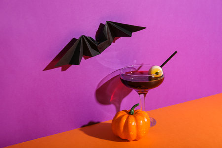 Glass of delicious cocktail, pumpkin, eye and paper bat for Halloween on color backgroundの写真素材