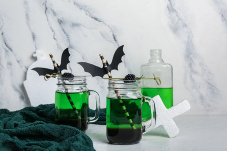 Mason jars of delicious green cocktail for Halloween with straws and paper bats on light backgroundの写真素材