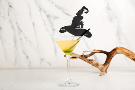 Glass of delicious cocktail for Halloween with paper hat and wood on light backgroundの写真素材