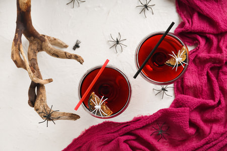 Glasses of delicious red cocktail for Halloween with spiders and wood on light backgroundの写真素材