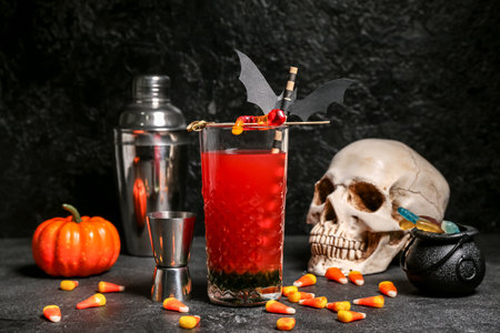 Glass of delicious red cocktail, measure cup, pumpkin and tasty candy corns for Halloween on dark backgroundの写真素材