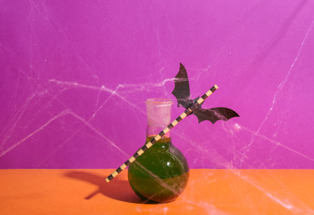 Test tube of delicious green cocktail with straw, paper bat and web for Halloween on color backgroundの写真素材