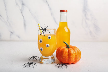 Glass and bottle of delicious orange cocktail for Halloween with spiders on light background, closeupの写真素材