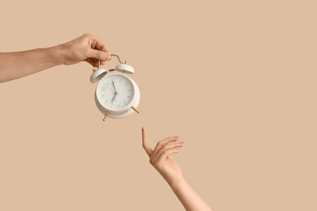 Hands holding alarm clock on beige backgroundの写真素材