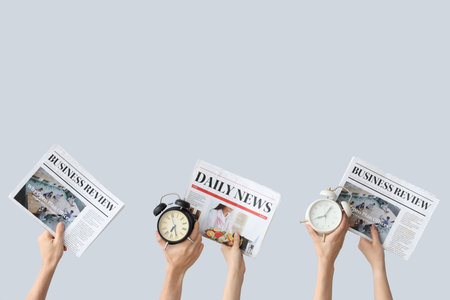 Hands holding different alarm clocks and newspapers on gray backgroundの写真素材
