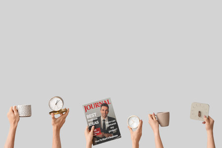 Hands holding alarm clocks, cups and magazine on gray backgroundの写真素材