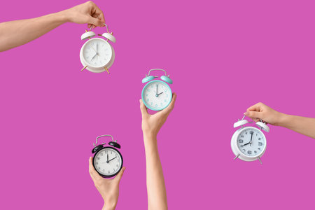 Hands holding different alarm clocks on purple backgroundの写真素材