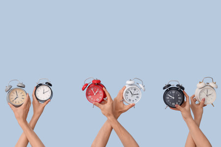 Hands holding different alarm clocks on blue backgroundの写真素材