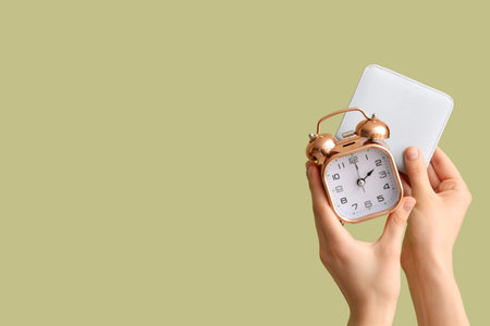 Female hands holding alarm clock and wallet on green background