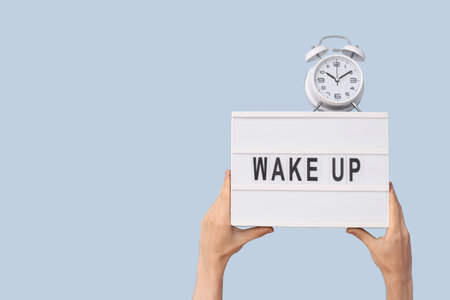 Male hands holding alarm clock and board with text WAKE UP on blue backgroundの写真素材