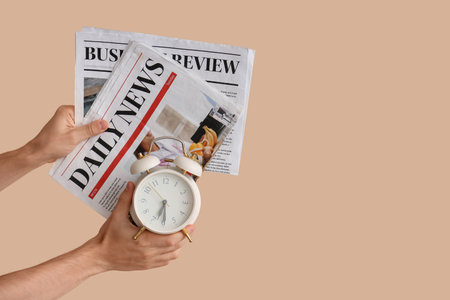 Male hands holding alarm clock and newspapers on beige backgroundの写真素材