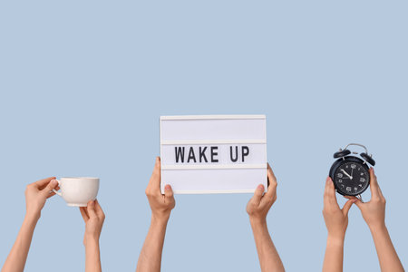 Hands holding alarm clock, cup and board with text WAKE UP on blue backgroundの写真素材