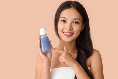 Young Asian woman pointing at bottle of micellar water on beige background, closeupの写真素材