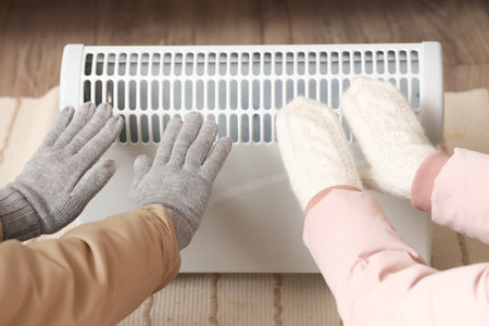 Young couple warming hands near radiator at home, closeupの写真素材