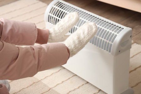Young woman warming hands in mittens near radiator at home, closeupの写真素材