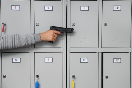 Male student with gun near locker, closeup. School shooting conceptの写真素材