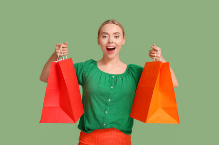 Happy young woman with shopping bags on green background