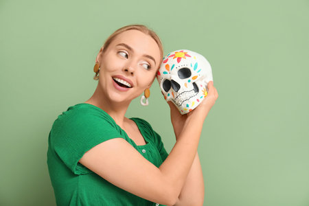 Pretty young woman with painted human skull on green background