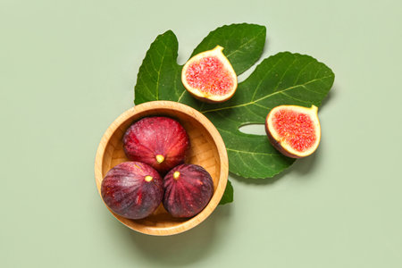 Bowl of ripe fresh figs with plant leaf on green backgroundの写真素材