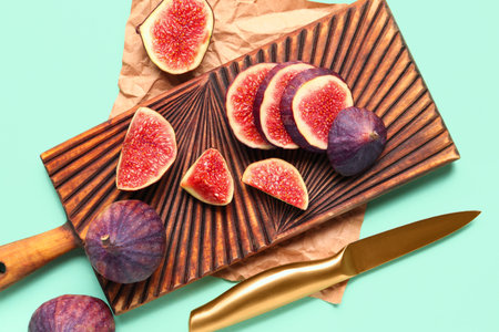 Wooden board with fresh juicy cut figs and knife on turquoise background