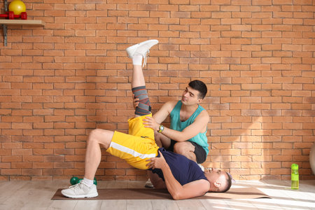 Mature man training on mat with therapist in rehabilitation center