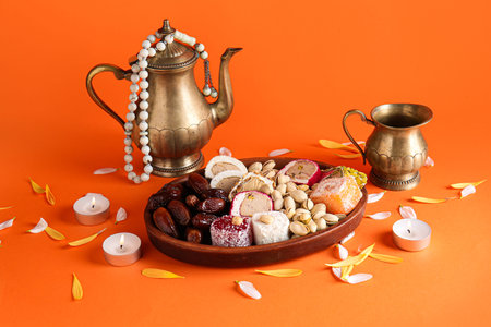 Teapot with candles, beads and plate of different treats on orange background. Divaly celebration