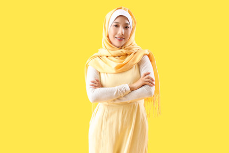 Beautiful young Asian woman in hijab on yellow backgroundの写真素材