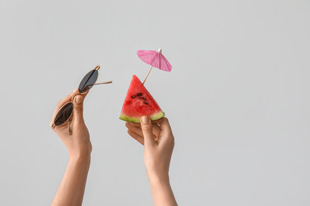 Female hands with slice of ripe watermelon, sunglasses and mini umbrella on white backgroundの写真素材