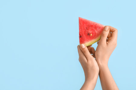 Female hands with slice of ripe watermelon on blue backgroundの写真素材