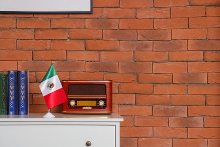 Retro radio receiver with Mexican flag and books on commode near brick wallの写真素材