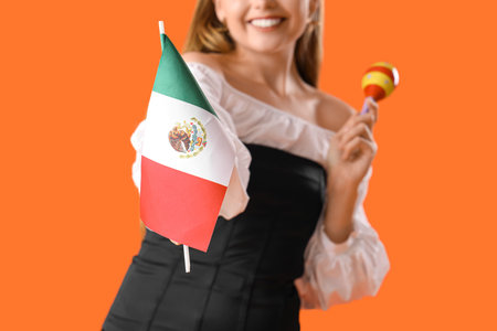 Young woman with Mexican flag and maraca on orange background, closeupの写真素材