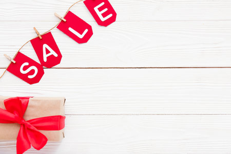 Gift box, rope, clothespins and flags with the word SALE on white wooden backgroundの写真素材