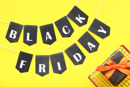 Shopping basket, gift box, rope and flags with text BLACK FRIDAY on yellow backgroundの写真素材