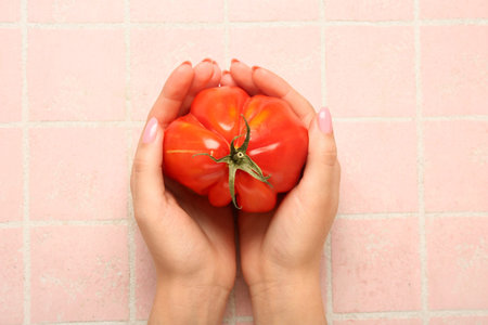 Female hands with fresh ripe tomato on pink tile backgroundの写真素材