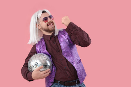 Handsome young man in wig with disco ball on pink backgroundの写真素材