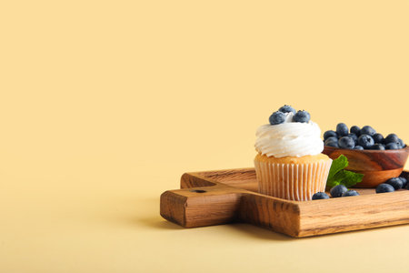 Wooden board of tasty cupcake with blueberries on yellow backgroundの写真素材