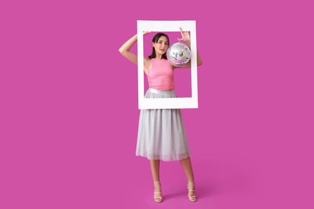 Beautiful young woman with disco ball and frame on purple backgroundの写真素材
