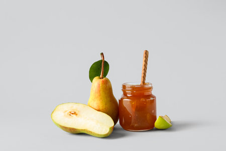 Glass jar of tasty pear jam with wooden spoon on white backgroundの写真素材